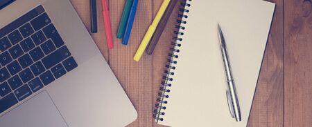 Opened blank notebook, laptop and colored felt-tip pens on the desktop.