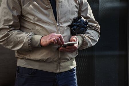 A man in a light jacket is looking for a way through the application in the phone.の写真素材