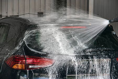 Black modern car being washed with pressure washer. jet of foam spraying onto car.の写真素材