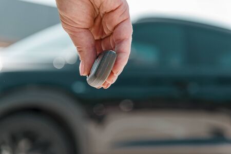 close-up woman hand presses a button on the car remote control against blur black car.の写真素材