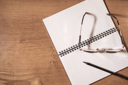 Opened notebook with black pencil and glasses on dark wooden table.