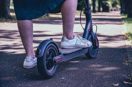 The woman uses a scooter. Women's legs on an electric scooter on the track in the park.の写真素材
