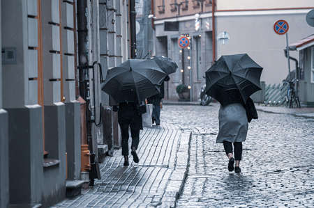 People walk down the street, hiding under umbrellas from the light rain in bad weather.の写真素材