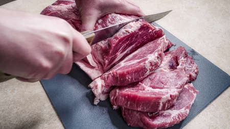 cutting raw meat on a cutting board. close-up of hands with knife and pork.の写真素材