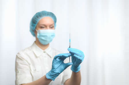 A blurred nurse wearing a mask and blue nitrile gloves holds a syringe with a vaccine. Selective focus.  vaccination concept.の写真素材