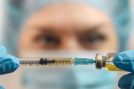 blurred background female scientist doctor in mask is typing a vaccine into a syringe. syringe with yellow liquidの写真素材