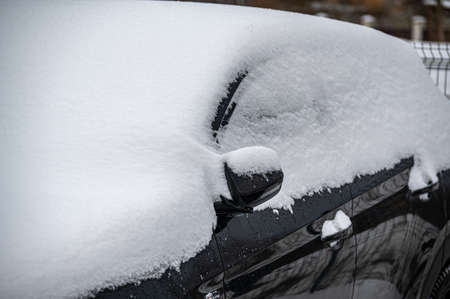 Black modern car covered with snow. Close-up of snowfall in winter.