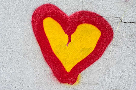 The symbol of love is painted on the gray plastered wall. Yellow-red heart on the wall of the house.の写真素材