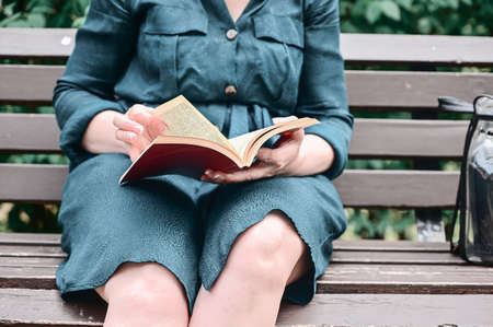 Close-up of a woman's hand reading a book while sitting on a park bench.の写真素材