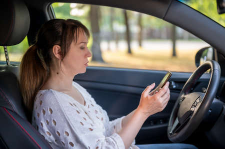 a woman uses a smartphone while sitting behind the wheel in her new car. woman driving.