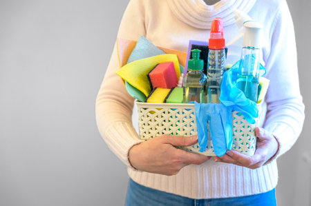 a woman holds a plastic basket with brushes, sponges and rubber gloves for cleaning the premises.の写真素材