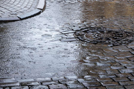 Large puddle on a cobbled street in the old town. Raindrops on the surface of a puddle.の写真素材