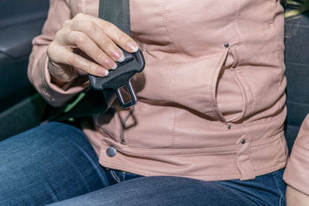 Close-up of a female passenger's hands trying to fasten their seat belt in a modern car.