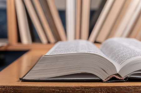 An open book on the background of a bookcase with books, hardback books on a wooden table. back to school.の写真素材