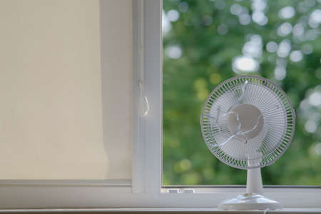 a working fan stands on the windowsill of an open window on a hot summer day.の写真素材
