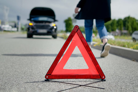 Red warning triangle and a woman walking towards her broken car on the road