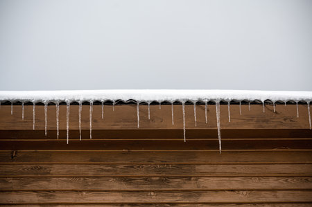 Icicles hanging from snow-covered roof of house. Cold winter outside the house.