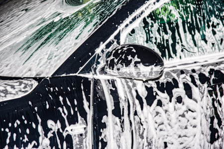 Hand washing the car with foam soap. The car is covered in foam.の写真素材