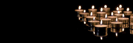 Several burning tea candles on reflective surface of dark mirror. Black background. There is an empty place for writing text. Panoramaの写真素材