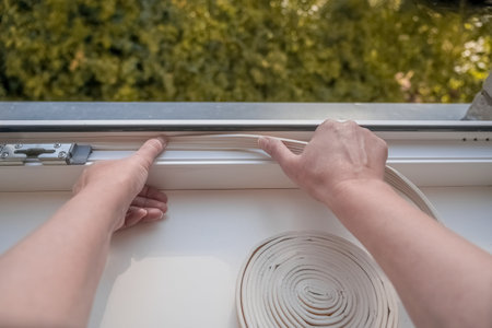 Installation of weatherproof insulation. worker sticking sealing foam tape on indoor windowの写真素材