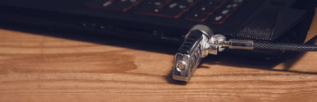 The black laptop is locked with a cable lock. Panorama of laptop connectors lying on a wooden table.の写真素材