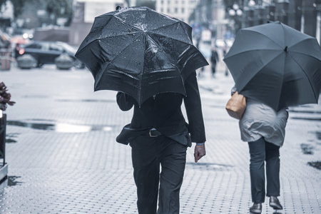 people with umbrellas walk down the street during the rain. people under black umbrellasの写真素材