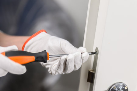 men's hands with a manual screwdriver and a screw handle on a white door. Door lock attachment.の写真素材