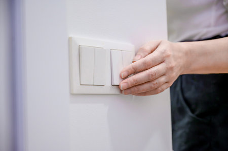 A woman turns off the home light switch when she leaves the room. Power, energy saving, energy saving.の写真素材