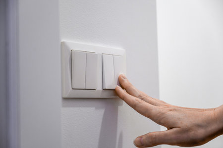 Close-up of a woman's finger turns on or off a light switch with a white wall at home. Power, energy, electricity saving.の写真素材