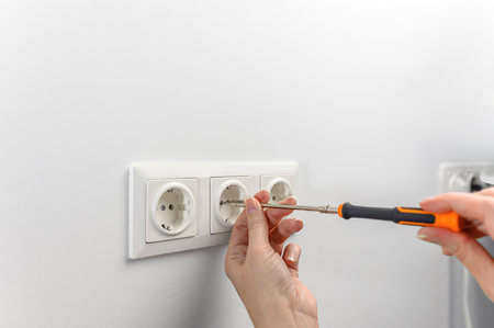 Close-up of the hands of an electrician holding a screwdriver, working with an electrical outlet in a residential electrical system.の写真素材