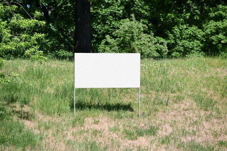 White board set on the ground with green grass against the background of trees and bushes outside on a summer dayの写真素材