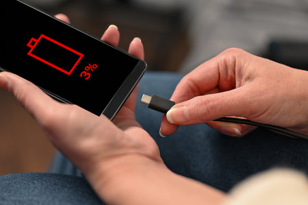 Charging smartphone via USB cable. Female hands hold a smartphone with a low battery. Wired chargingの写真素材