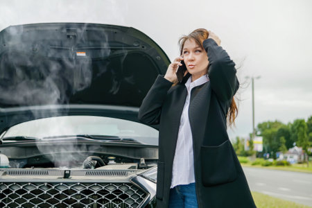 a woman is talking on a mobile phone next to a broken car. Calls technical assistance on the road.の写真素材