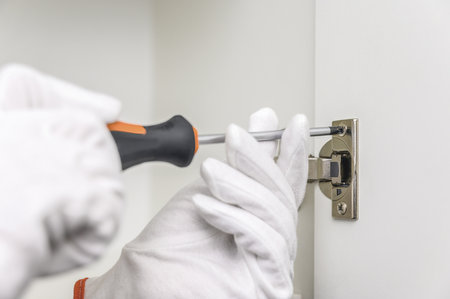 A man in gloves using a screwdriver assembles new kitchen furniture at his home. a person in white gloves holding a screwdriverの写真素材