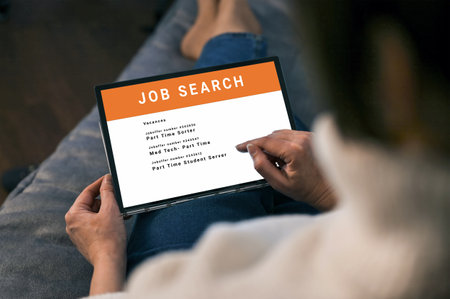 Woman browsing job opportunities online using tablet application for job search. unemployed job seeker looking for new vacancies on website page on tablet screen, hiring concept, rear viewの写真素材