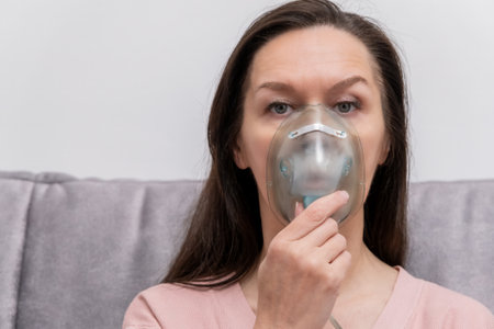 The woman inhales the respiratory tract and lungs when applying drugs. A woman breathes through a face mask using a nebulizer.の写真素材