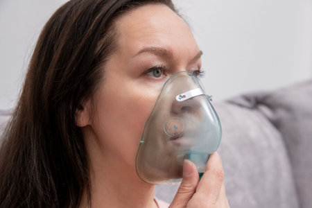 Sick woman doing inhalation using oxygen mask. Unhealthy girl suffer from serious viral illness.の写真素材