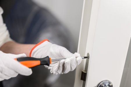 home renovation concept. A gloved repairman's hand adjusts the door mechanism with a screwdriver.の写真素材