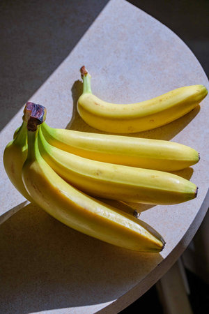 A bunch of organic ripe bananas sits on the kitchen table in the sun.の写真素材