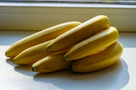 On a white windowsill there is a bunch of ripe yellow bananas. bananas in backlight.の写真素材