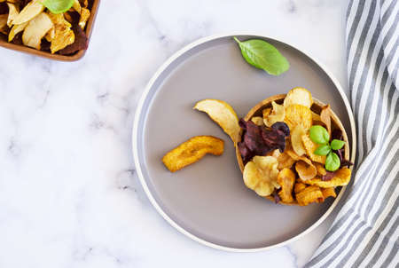 Vegan snacks, multicolored vegetable and fruits chips in wooden bowl , selective focus. Flat lay. Bowl of healthy vegetable chips from beets, sweet potatoes,apples, oranges and carrotsの写真素材