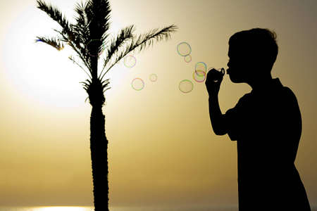 Boy playing with soap bubbles, summer, tree, sea, night の写真素材