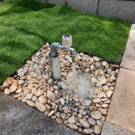 Outdoor water faucet running over decorative garden pebbles and artificial grassの写真素材