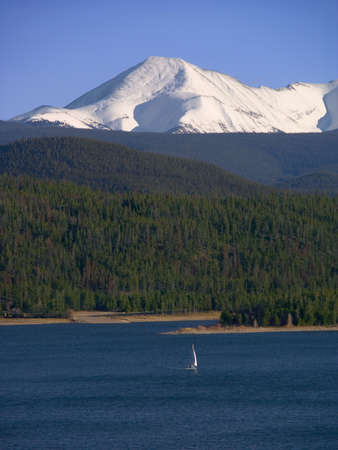 A lone sailboat ventures out while the snow-covered Rockies provide a backdropの写真素材