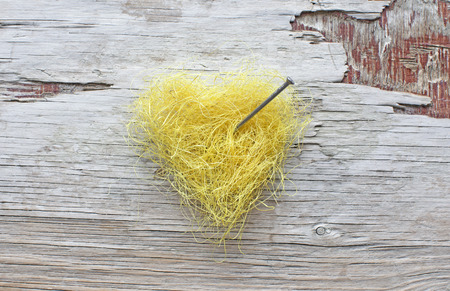 Yellow vintage heart pierced by nail and placed on a scratched wood background