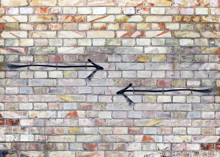 Background of old vintage color brick wall with two opposite black arrowsの写真素材