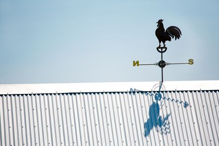 Rooser Weather Vane Atop Tin Roof in Clear Blue Skyの写真素材