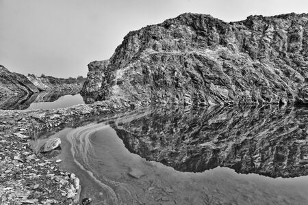Black and white nature view of a rock mountain from an abondon mine with its reflection from the man made lakeの写真素材