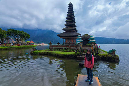 Bratan Lake, Bali - November 25th, 2017: A female muslim woman in hijab taking photo in front of the floating tample at Bratan Lake. Bratan lake is of of the famous Bali tourism spotのeditorial素材