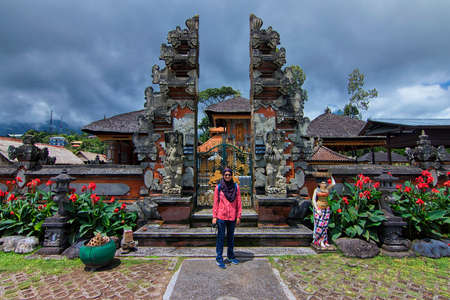 Bratan Lake, Bali - November 25th, 2017: A female muslim woman in hijab taking photo in front of unique architectural gate at Bratan Lake. Bratan lake is of of the famous Bali tourism spotのeditorial素材